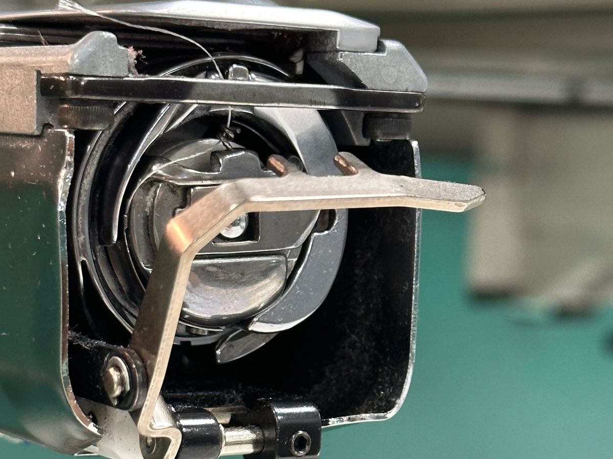 Close-up of a rotary hook and thread catcher lever on a teal machine