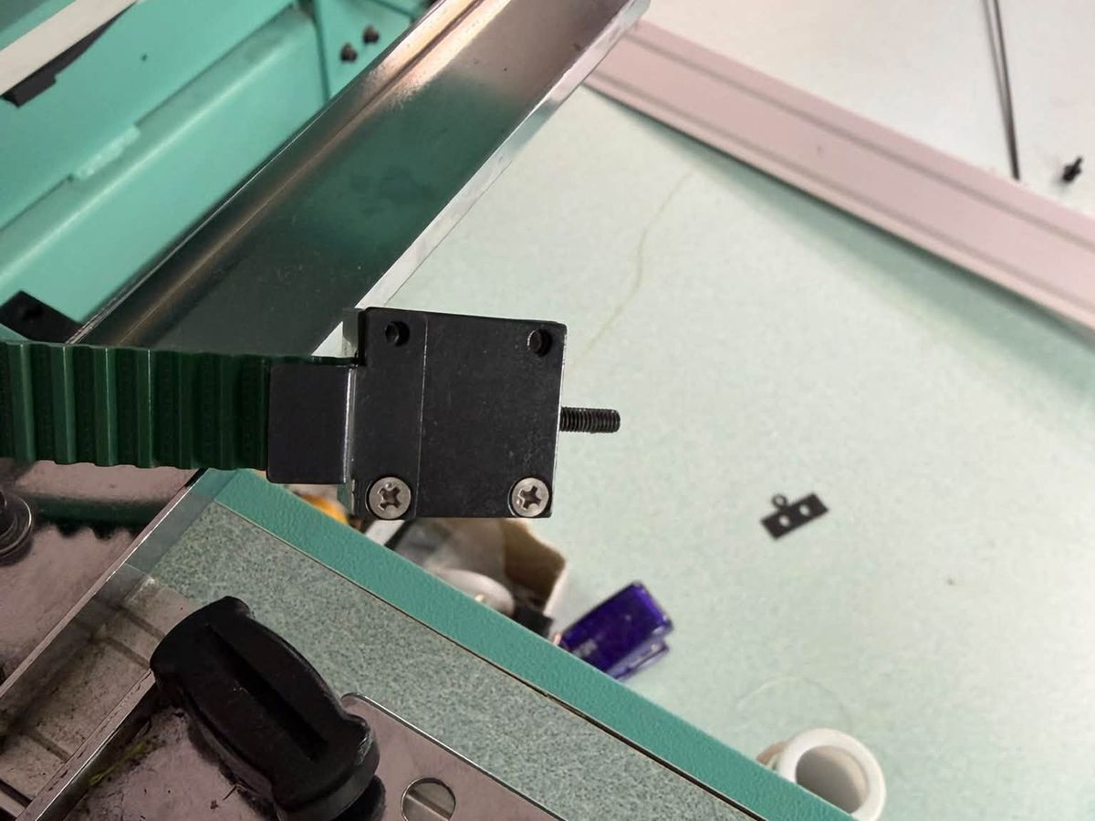 Green timing belt ending in a black clamp block above a chrome pantograph plate