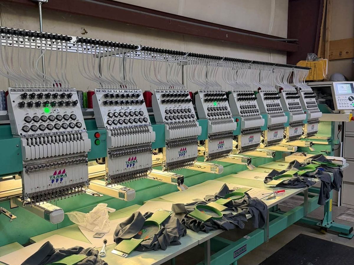 Eight-head Tajima in a metal-walled shop with gray shirts hooped in green frames
