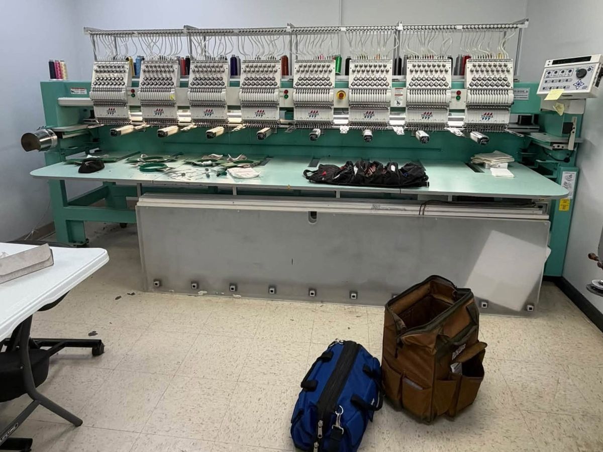 Eight-head Tajima in a small white room with tool bags on the floor in front