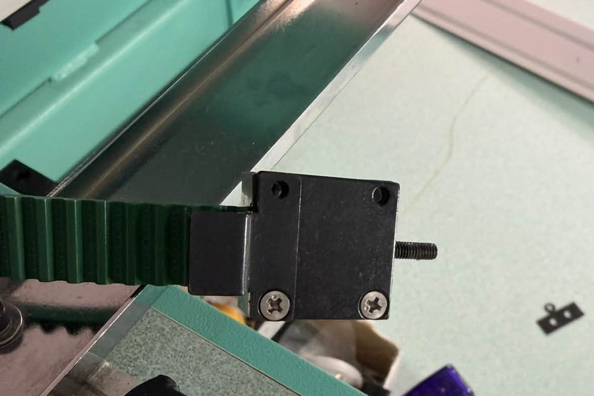 Green toothed belt running into its black clamp block on an embroidery machine frame drive with the cover off