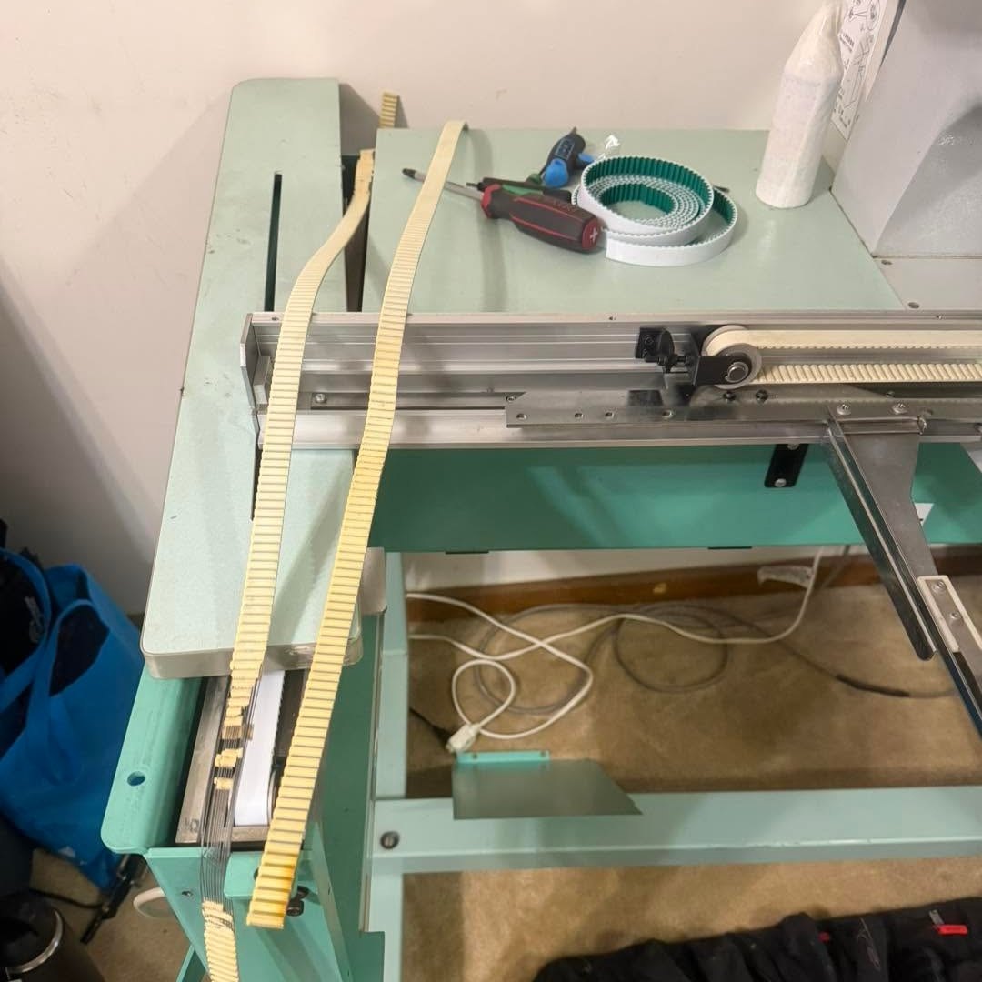 Old toothed belts draped over an embroidery machine frame beside a new replacement belt