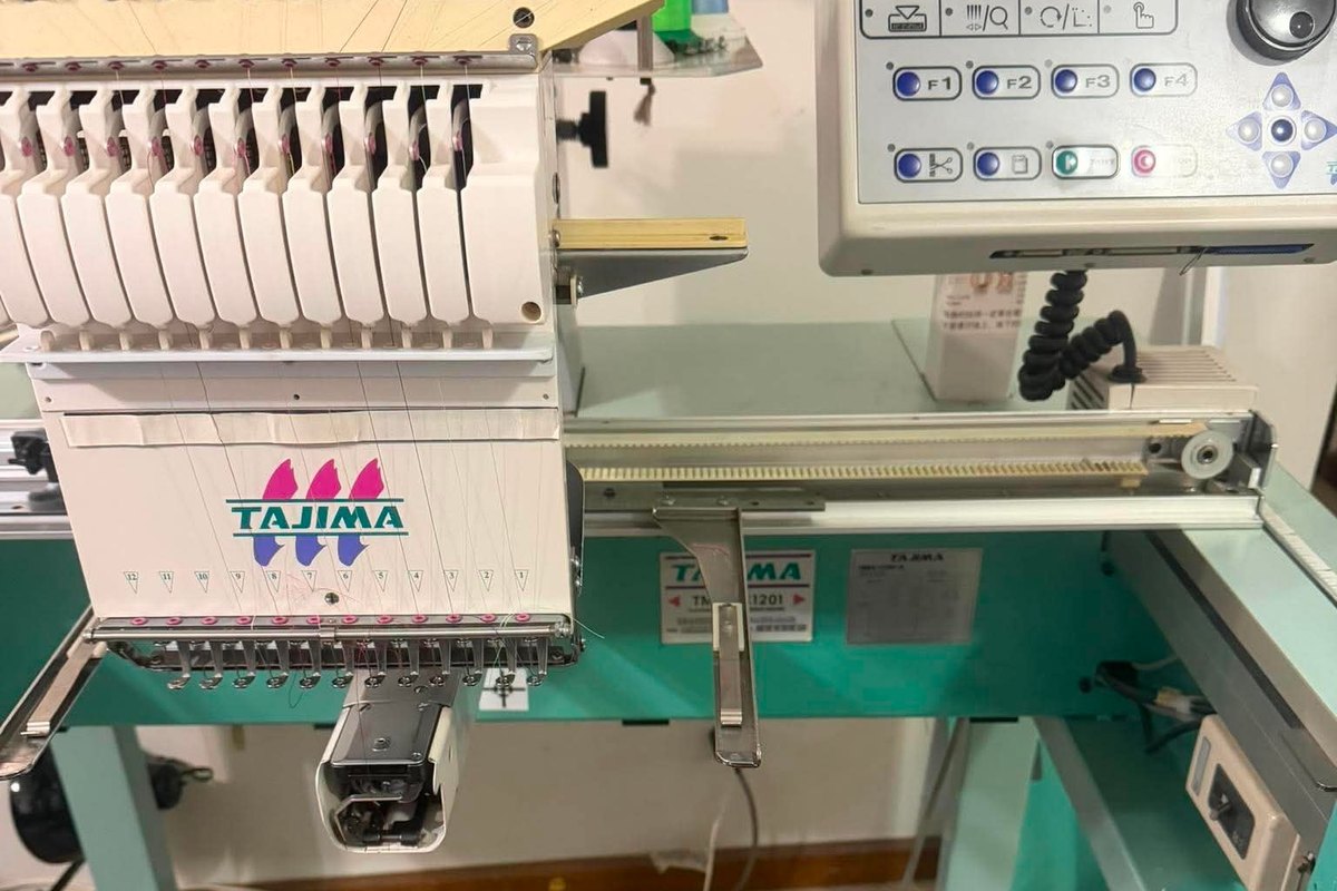Tajima single-head with its control panel and X-axis rail on a teal stand