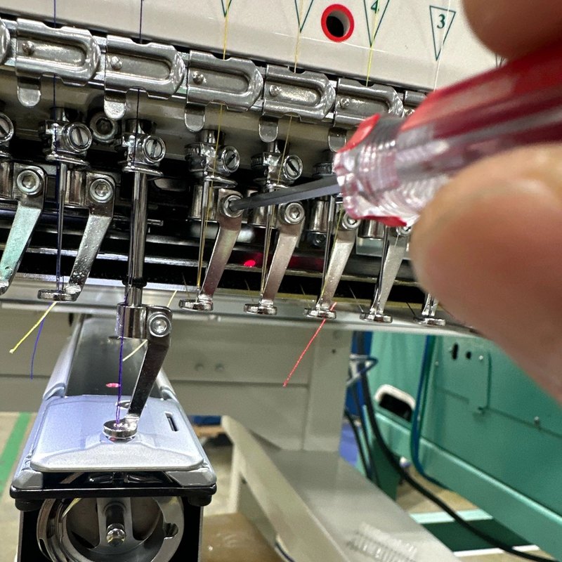 Hand adjusting a needle bar screw on a multi-needle embroidery head