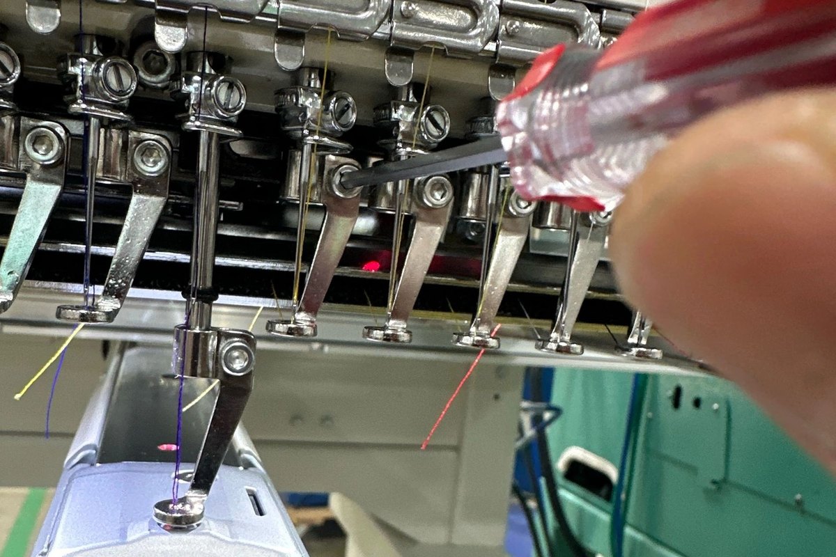 Driver turning a needle bar screw beside a row of presser feet