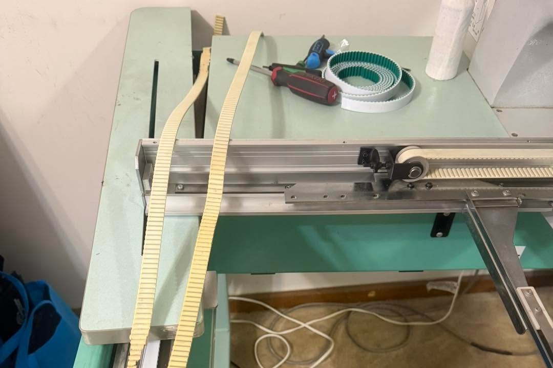 Worn toothed belts pulled from an embroidery machine frame beside a coiled new timing belt and two screwdrivers