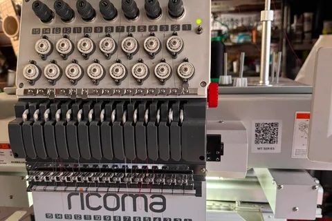 Ricoma fifteen-needle sewing head with its tension knobs, needle bars, and Ricoma name plate
