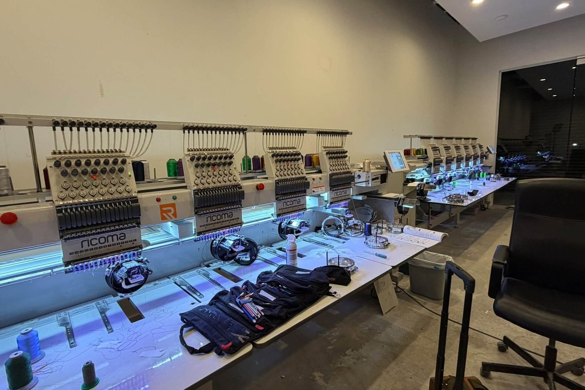 Row of Ricoma embroidery heads lit blue, with tool rolls and hoops on the table