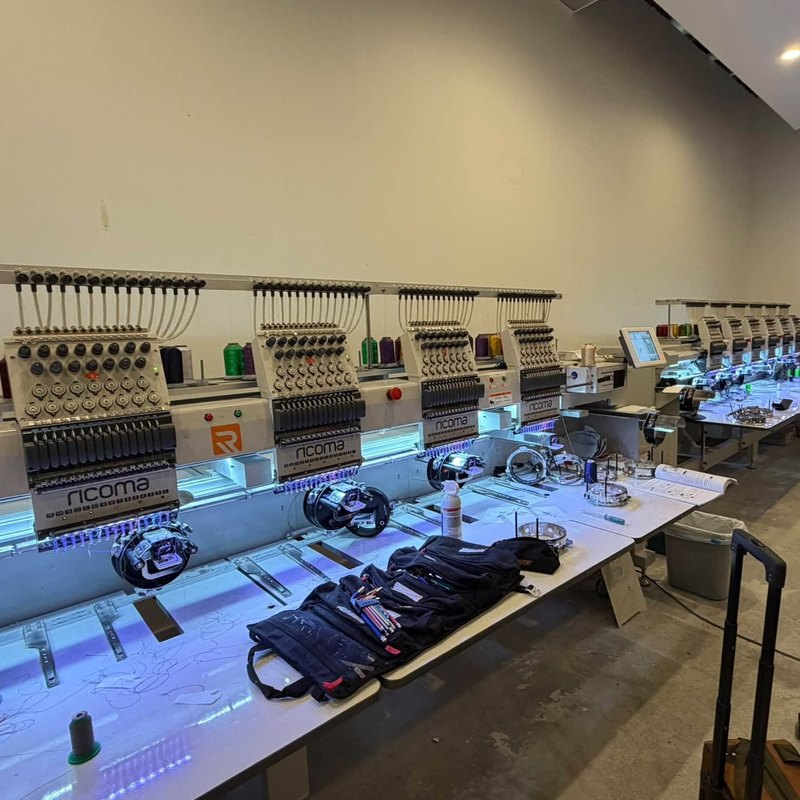 Ricoma multi-head sewing heads lined up under blue work lights