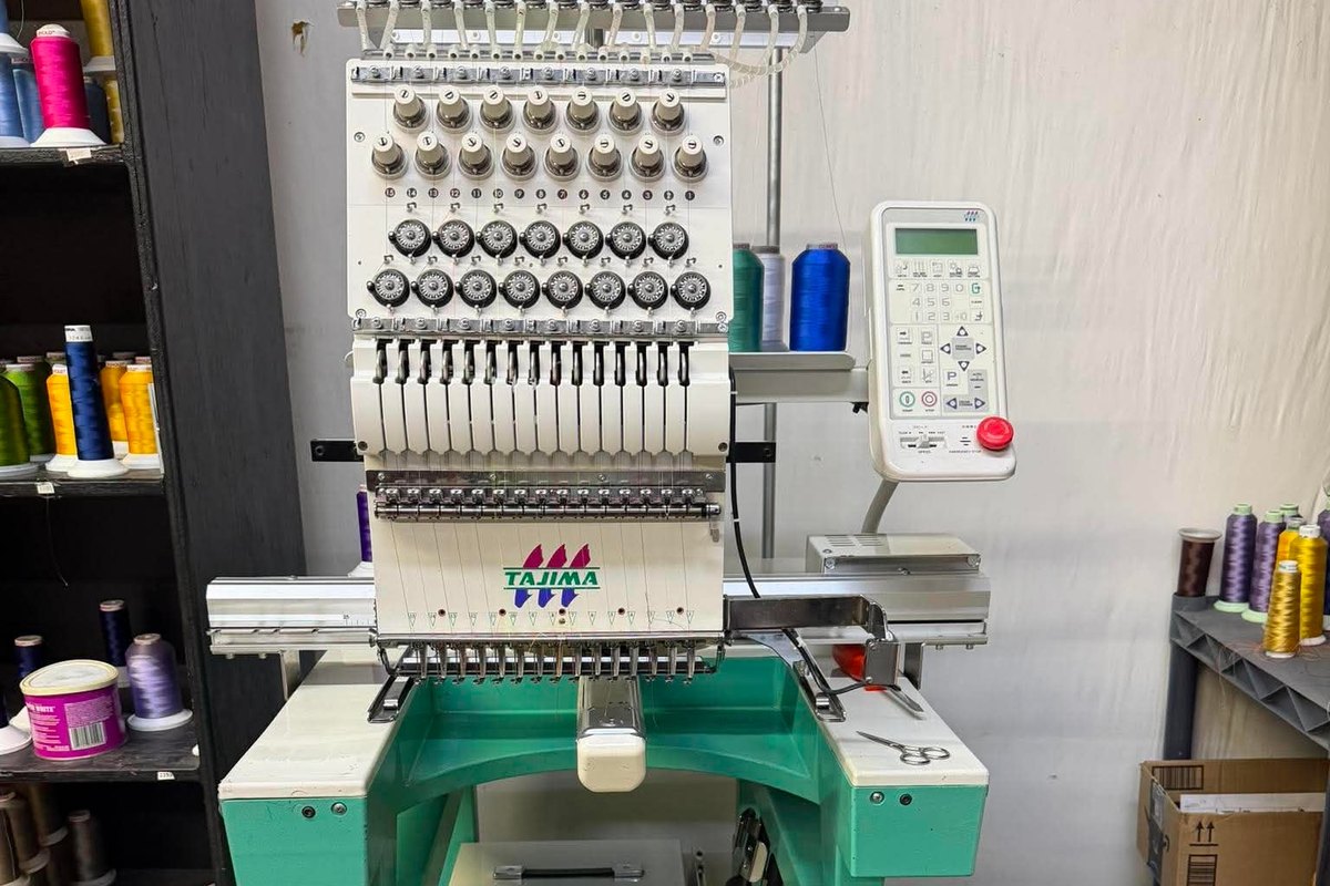 Tajima single-head embroidery machine on a teal stand in a thread-lined shop